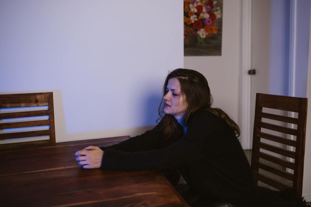 A woman sitting alone at a dining room table while thinking.