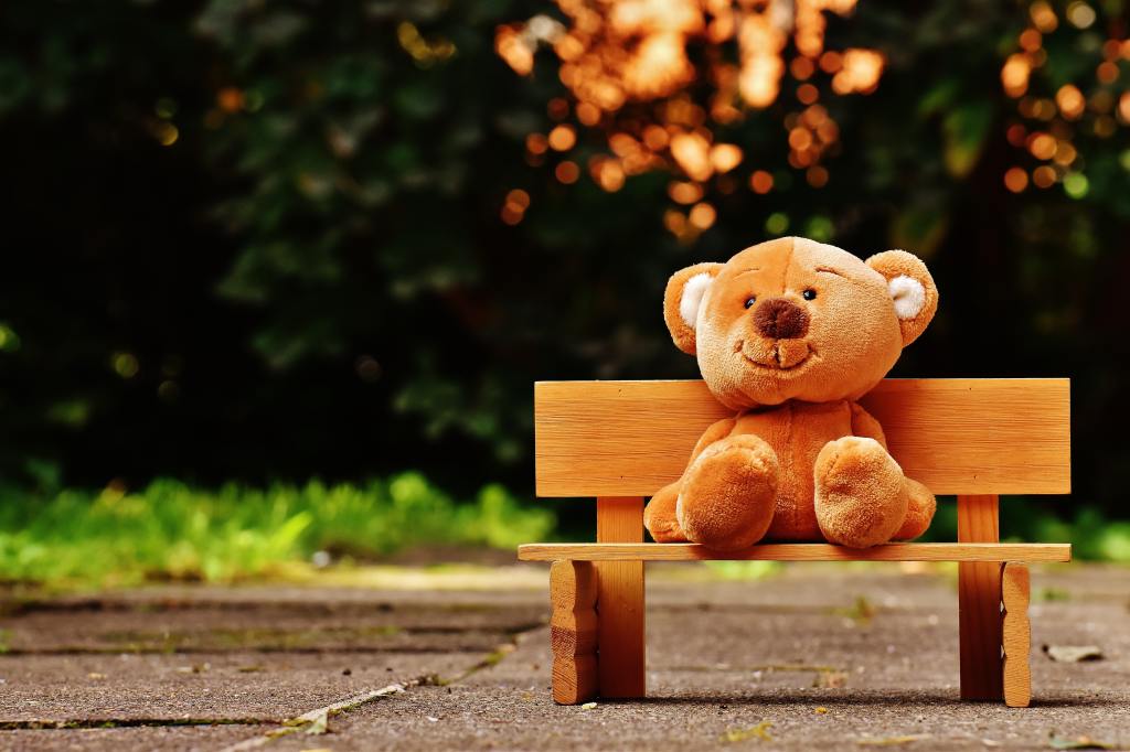 A stuffed bear toy sitting on a small bench.